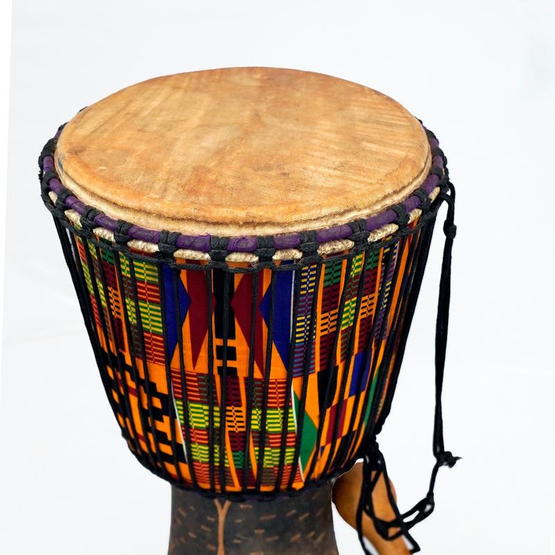 A djembe drum wrapped in colourful kente-style cloth, with a beaded shaker